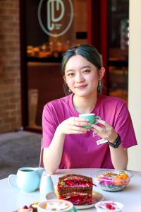 plume cafe employee holding specialty coffee with rainbow sandwich and breakfast bowl